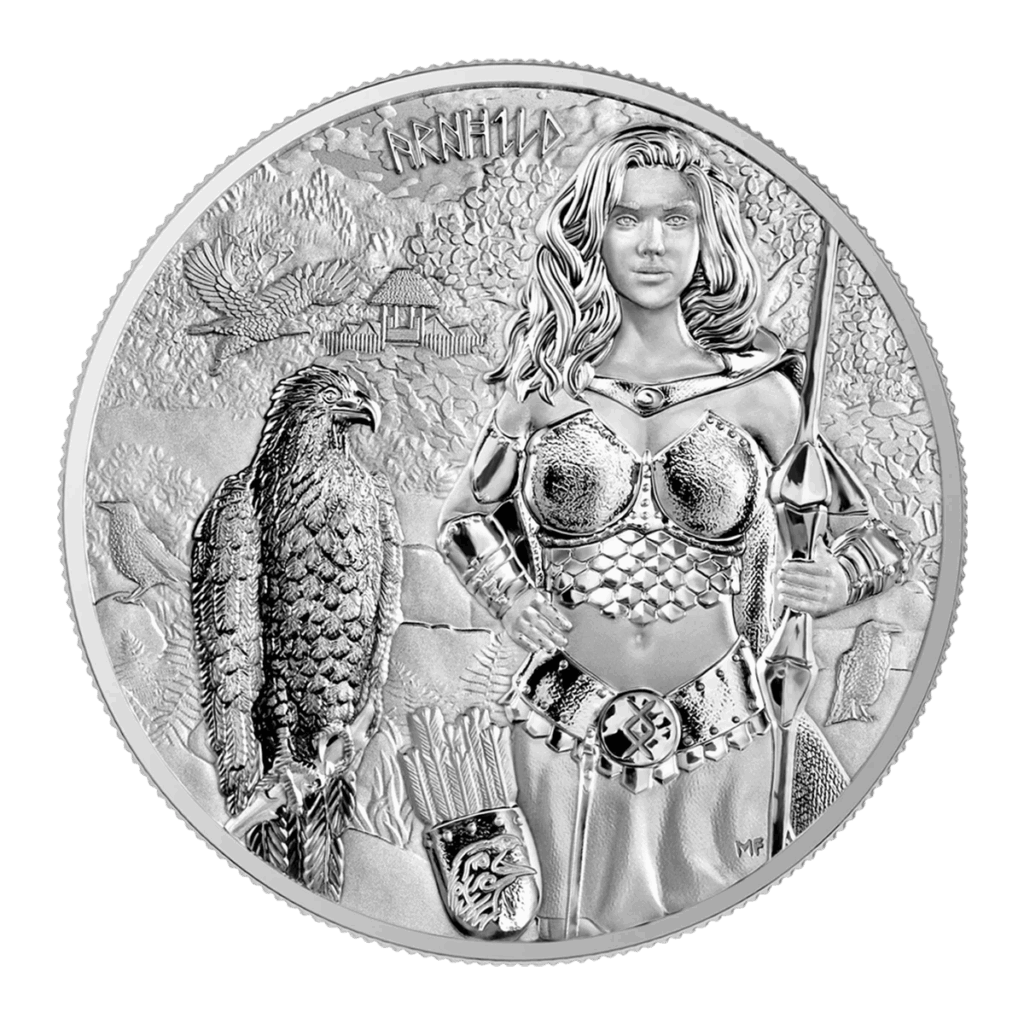 La moneta 2025 Valchirie: Arnhild 1 oz Argento Fior di Conio presenta una donna guerriera in armatura con lancia e aquila, con montagne, alberi, case e simboli runici incisi sopra la testa.