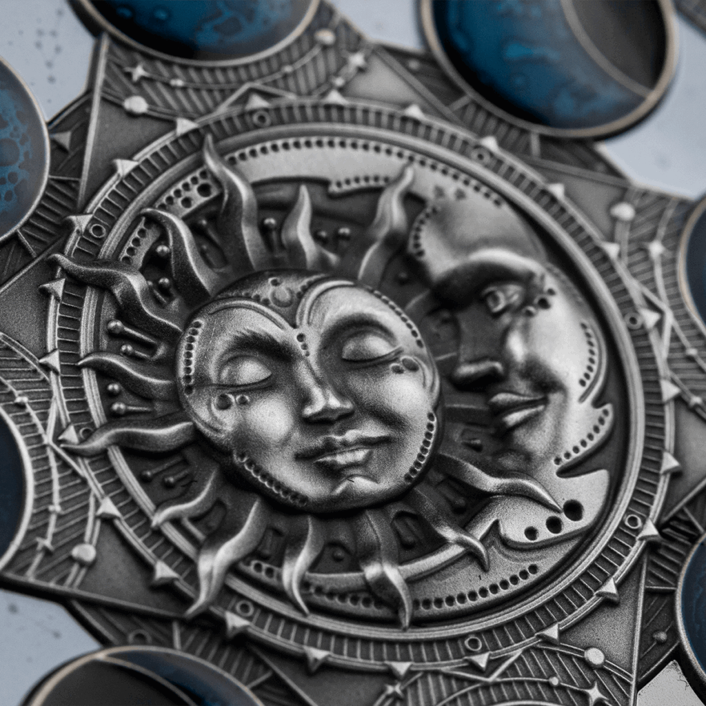 Il Calendario Lunare 2 Dollari presenta un rilievo metallico di facce del sole e della luna intrecciate, accentuate da forme di mezzaluna blu e motivi celestiali per un look ornato e mistico.